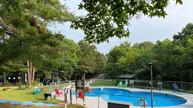 A backyard with a swimming pool, surrounded by a fence, and featuring outdoor furniture and trees. - RV Site #38 Pull Through (Hardin)