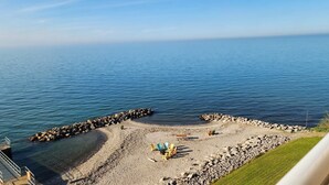 En strand med en stenig kustlinje, klart blått vatten och en pir som sträcker sig ut i havet.