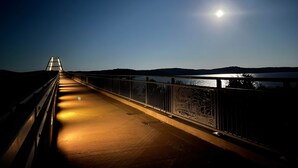 A nighttime view of a bridge with a metal railing, a lit pathway, and a body of water in the distance. - RV Site #39 Pull Through (Hardin)