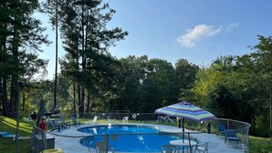 A fenced outdoor swimming pool with a deck, lounge chairs, and a colorful umbrella. - RV Site #39 Pull Through (Hardin)