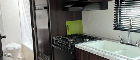 A compact kitchen with dark wooden cabinets, a black stove, a microwave, and a sink.