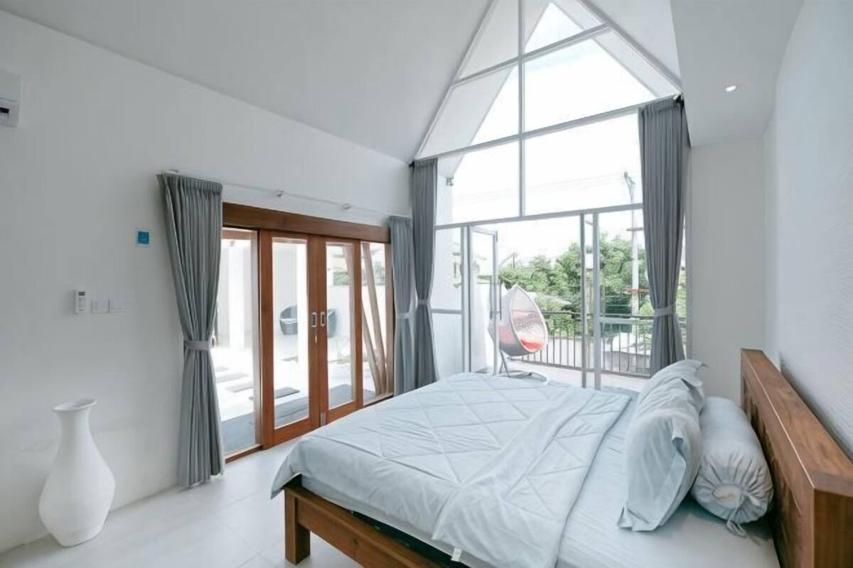 Een slaapkamer met een groot bed, uitzicht door een glazen deur en een witte vaas.