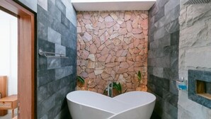Une salle de bain moderne dotée d’une baignoire originale en forme de cœur, d’un mur en pierre et d’une porte en bois.