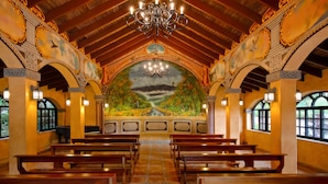 An interior with wooden pews, a mural, and ornate ceiling details.