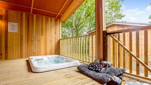 Une terrasse en bois avec un jacuzzi, un panier pour chien et un espace clôturé.