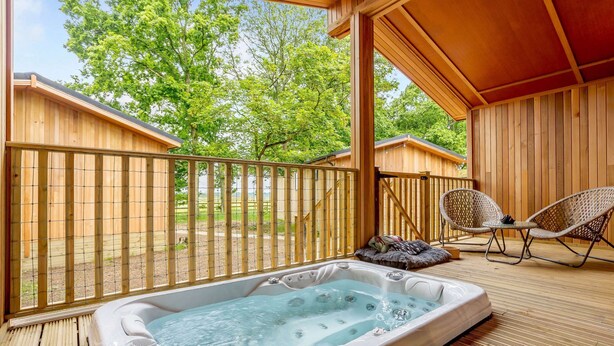Une terrasse en bois avec un jacuzzi, des fauteuils en osier et une vue sur les arbres.