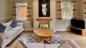 A living room with a white sofa, a round wooden coffee table, a flat-screen TV, and a painting on the wall. - Holiday Lodge in The Cotswolds (Kingham)