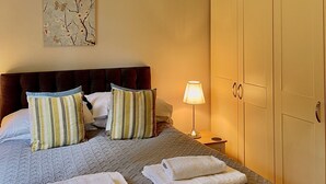 A neatly made bed with pillows and towels, a bedside lamp, and a wardrobe. - Holiday Lodge in The Cotswolds (Kingham)