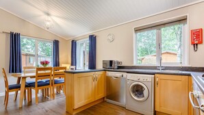 A kitchen with wooden cabinets, a washing machine, a microwave, and a dining area with a table and chairs. - Holiday Lodge in The Cotswolds (Kingham)