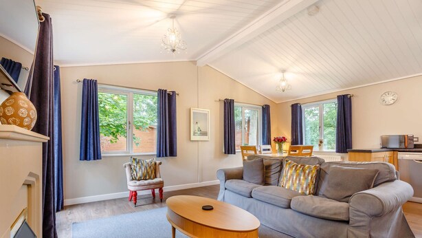 A modern living room with a grey sofa, a wooden coffee table, and a dining area with a table and chairs. - Holiday Lodge in The Cotswolds (Kingham)