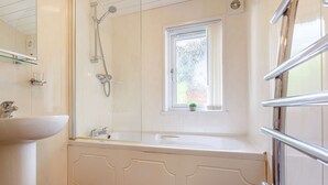 A bathroom with a white sink, a glass shower enclosure, and a window with a plant. - Holiday Lodge in The Cotswolds (Kingham)