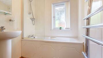 Une salle de bain avec un lavabo blanc, une douche en verre et une fenêtre agrémentée d’une plante.