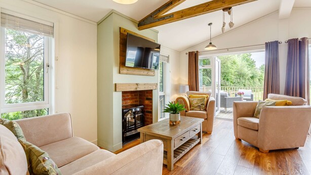 A cozy living room with a fireplace, comfortable seating, and a balcony with curtains. - Holiday Lodge in The Cotswolds (Kingham)