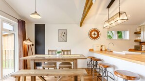 A modern kitchen with wooden countertops, a dining area with a bench, and bar stools. - Holiday Lodge in The Cotswolds (Kingham)