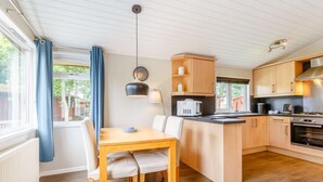 A modern kitchen with wooden cabinets, a central island, and a dining area with a table and chairs. - Holiday Lodge in The Cotswolds (Kingham)