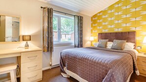 A bedroom with a bed, a desk, and a window with curtains. - Holiday Lodge in The Cotswolds (Kingham)