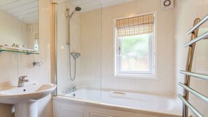 A modern bathroom with a white sink, a bathtub, and a shower. There is a window with a grid pattern and a towel rack on the right. - Holiday Lodge in The Cotswolds (Kingham)