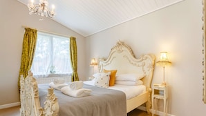 Ein Schlafzimmer mit einem großen, verzierten Bett, zwei Nachttischlampen und einem Fenster mit Vorhängen.