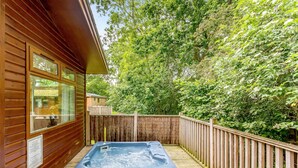Una terraza de madera con un jacuzzi, rodeada por una valla de madera y abundante vegetación.