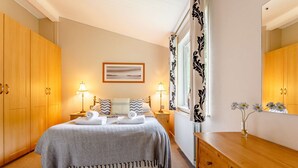 Un dormitorio ordenado con cama, lámparas de noche, cómoda y ventana con cortinas.