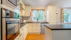 Una cocina moderna con armarios blancos, electrodomésticos de acero inoxidable, piso de madera y una ventana con vista a zonas verdes.