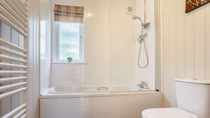 Un baño con bañera, inodoro y una ventana con una planta.