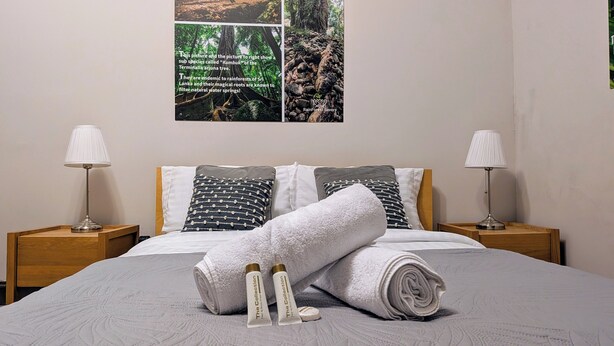 A neatly made bed with a rolled towel and two bottles, two nightstands with lamps, and a wall with three framed pictures.