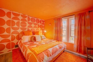 Een slaapkamer met een bed, oranje gordijnen en een raam met uitzicht.