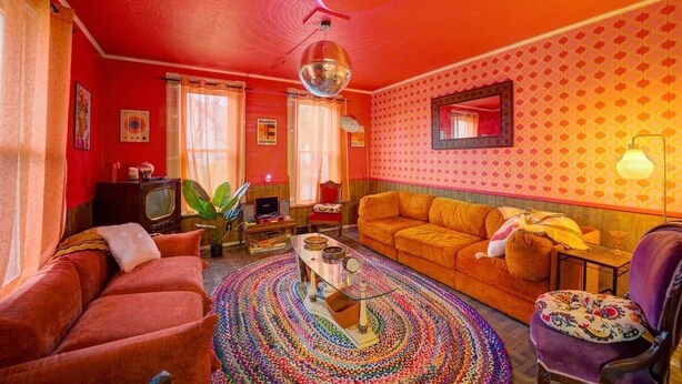 A retro-styled living room with a vibrant red color scheme, a round coffee table, a sofa, and a patterned rug. - 4 BR Home 5 Mins to Cedar Point, Retro 1970s! (Sandusky)