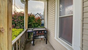 A covered porch with a Blackstone grill, wooden railing, and a view of a house and trees. - 4 BR Home 5 Mins to Cedar Point, Retro 1970s! (Sandusky)