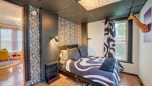 A bedroom with a zebra-patterned wall, a bed with a patterned bedspread, a giraffe decoration, and a window with curtains. - 4 BR Home 5 Mins to Cedar Point, Retro 1970s! (Sandusky)