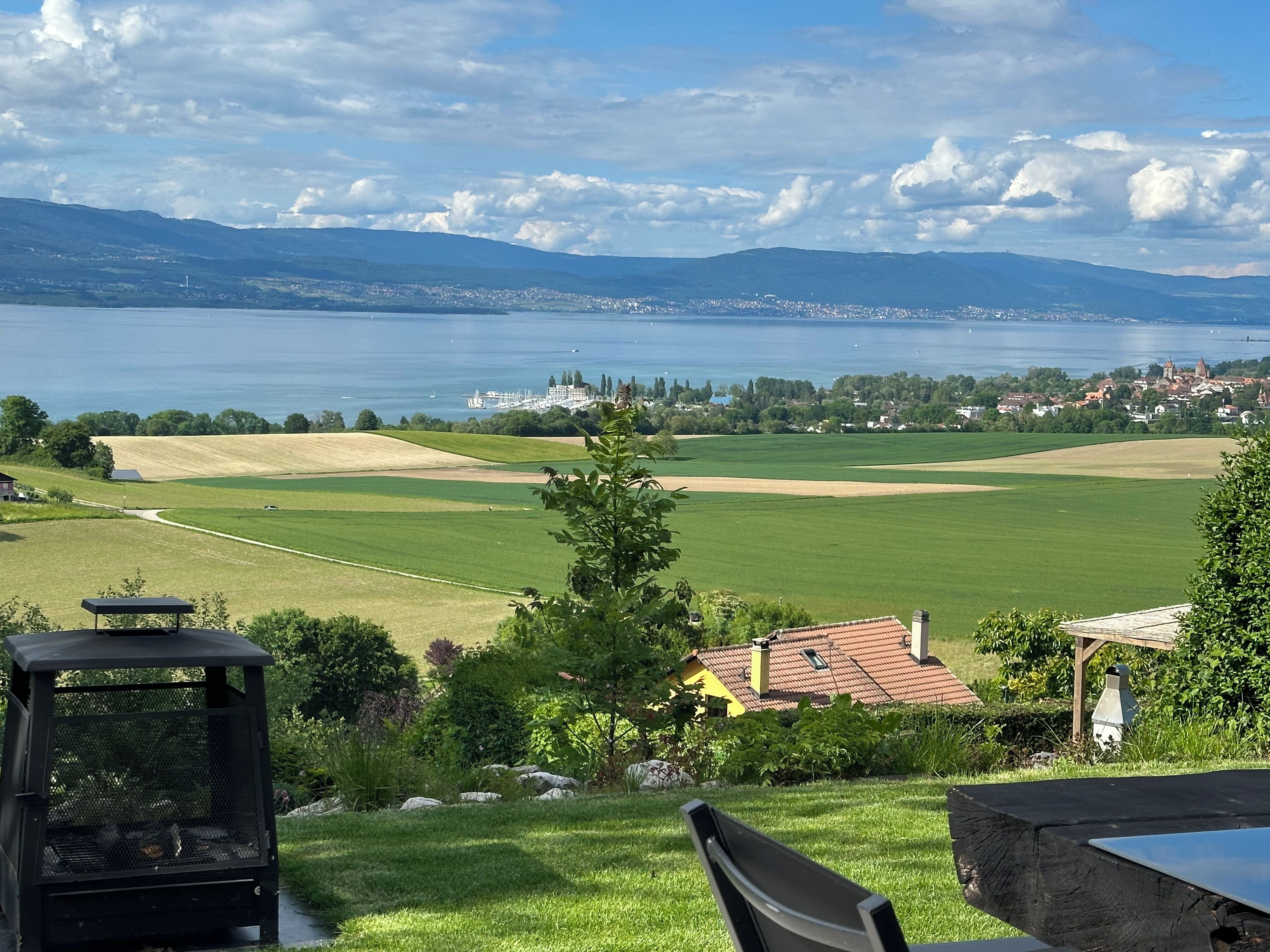 A view of a lake with a distant town, green fields, and a gazebo.