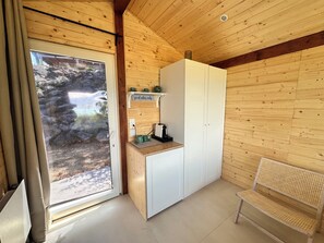 A wooden interior with a kitchenette, a bench, and a door leading to an outdoor area.