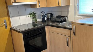 A modern kitchen with wooden cabinets, a black oven, a stainless steel sink, and a window with blinds.