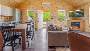 A cabin interior with a dining area, a sofa, a fireplace, and a TV. - Hot Tub~Firepit~Riverfront~Near Lake Cumberland (Jamestown)