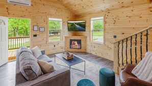 A cozy wooden cabin interior with a sofa, a coffee table, a fireplace, and a TV mounted on the wall. - Hot Tub~Firepit~Riverfront~Near Lake Cumberland (Jamestown)