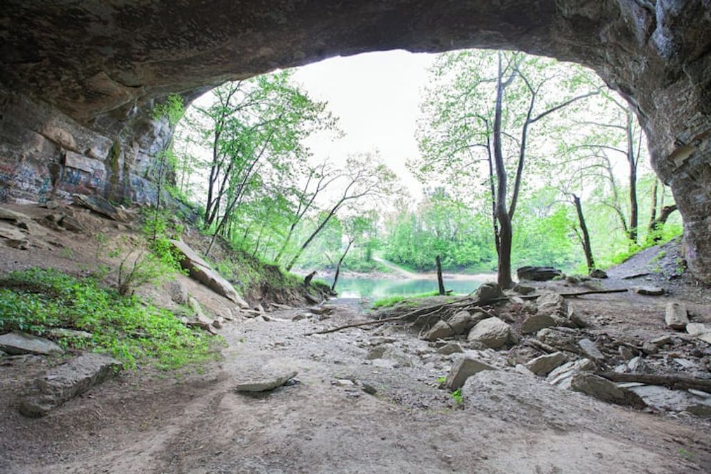 Ein natürlicher Höhleneingang mit einem Feldweg, der in einen bewaldeten Bereich führt.