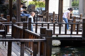 A wooden deck with a railing, a pond with fish, and outdoor seating. - Sanhe International Hotel (Jinhu)