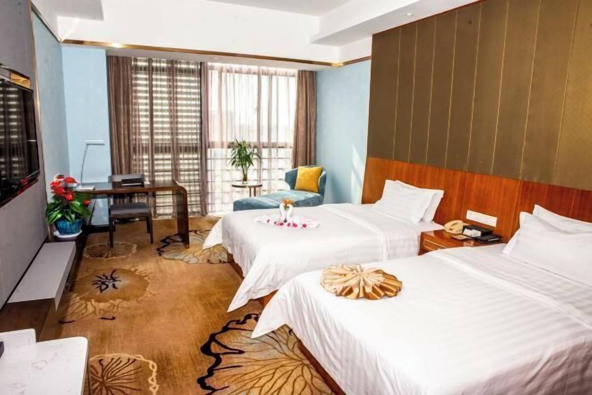 A hotel room with two beds, a desk, a chair, a TV, and a window with curtains.