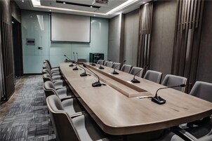 Un salón de conferencias con una larga mesa, varias sillas, micrófonos y una pantalla de proyector.