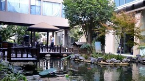 A tranquil outdoor pond with a wooden deck and seating area, surrounded by rocks and plants. - Sanhe International Hotel (Jinhu)