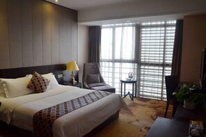 A hotel room with a large bed, a chair, a small table, and a TV.