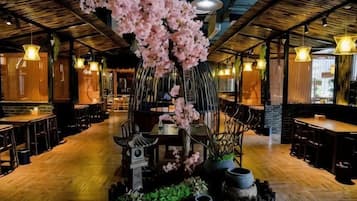 A restaurant interior with wooden flooring, tables, chairs, hanging lights, and a central decorative tree.