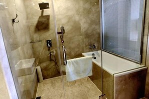A modern bathroom with a glass shower enclosure, a white bathtub, and a marble-tiled floor.