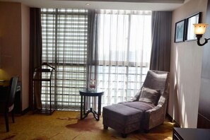 A hotel room with a large window, a chair, a small table, and a lamp.