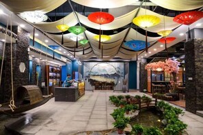 Um hall de hotel com balcão de recepção, área de estar, um pequeno jardim interno e um mural na parede.
