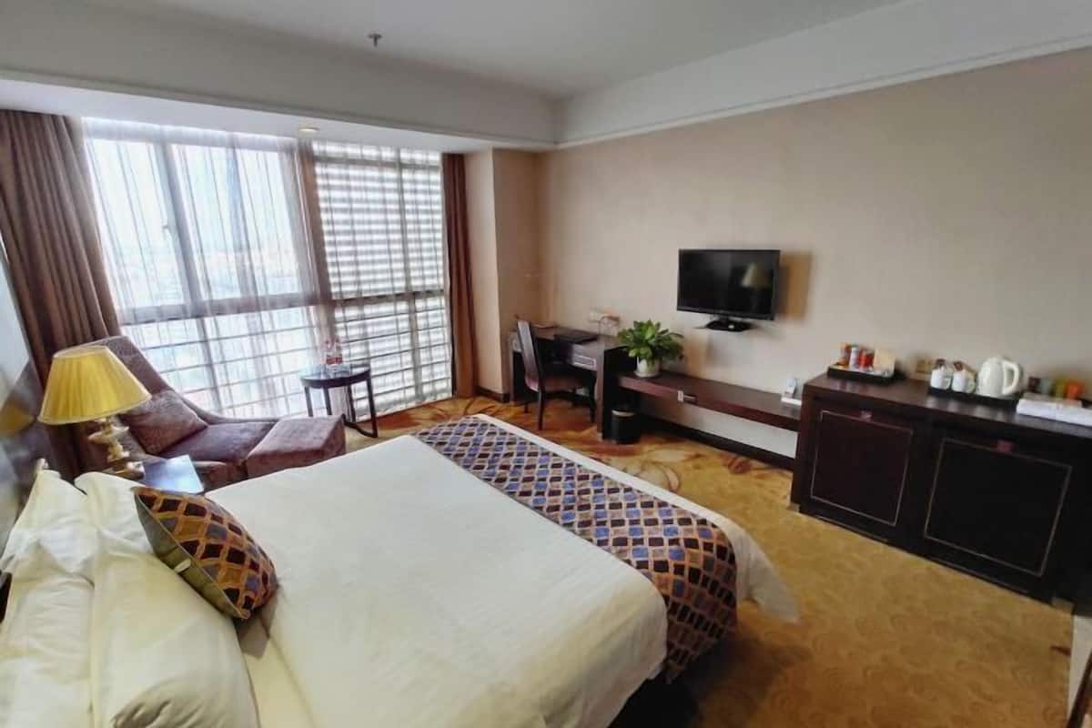 A hotel room with a bed, a desk, a television, and a window with curtains.
