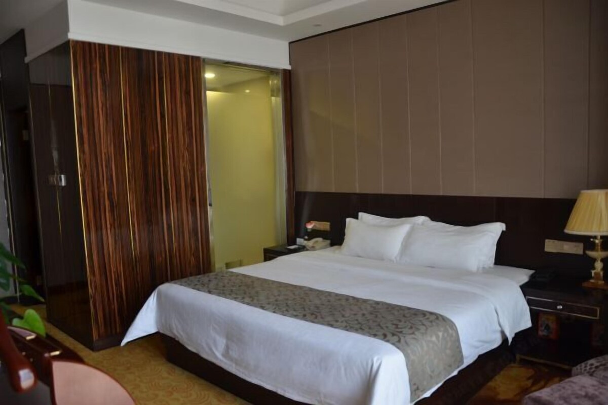 A hotel room with a large bed, a nightstand, a lamp, and a wardrobe.