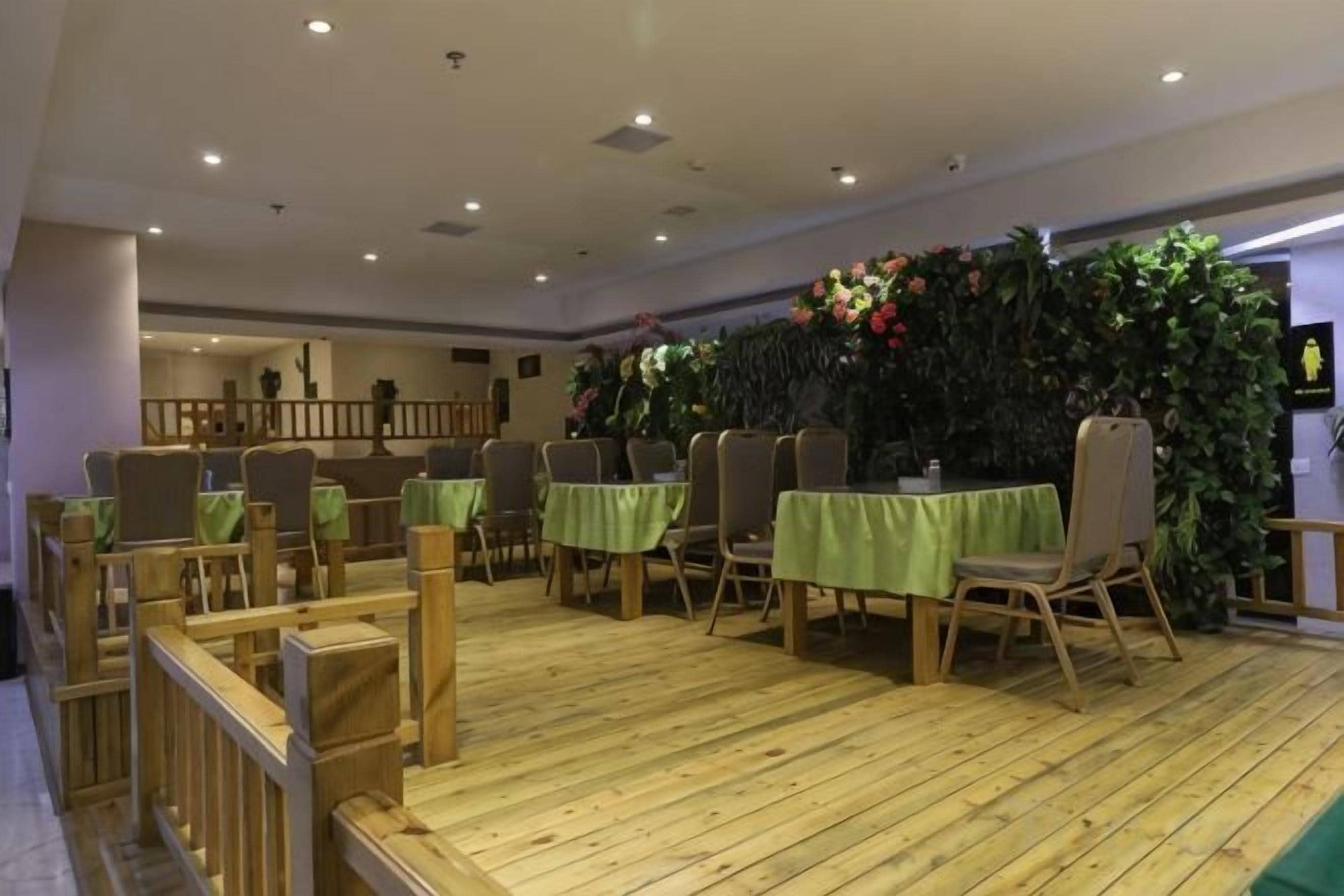 A dining area with tables and chairs, a wooden floor, and a decorative wall with plants.