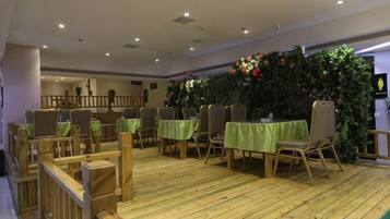 A dining area with tables and chairs, a wooden floor, and a decorative wall with plants.